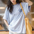Person wearing a light blue t-shirt with text, holding a yellow bag indoors.